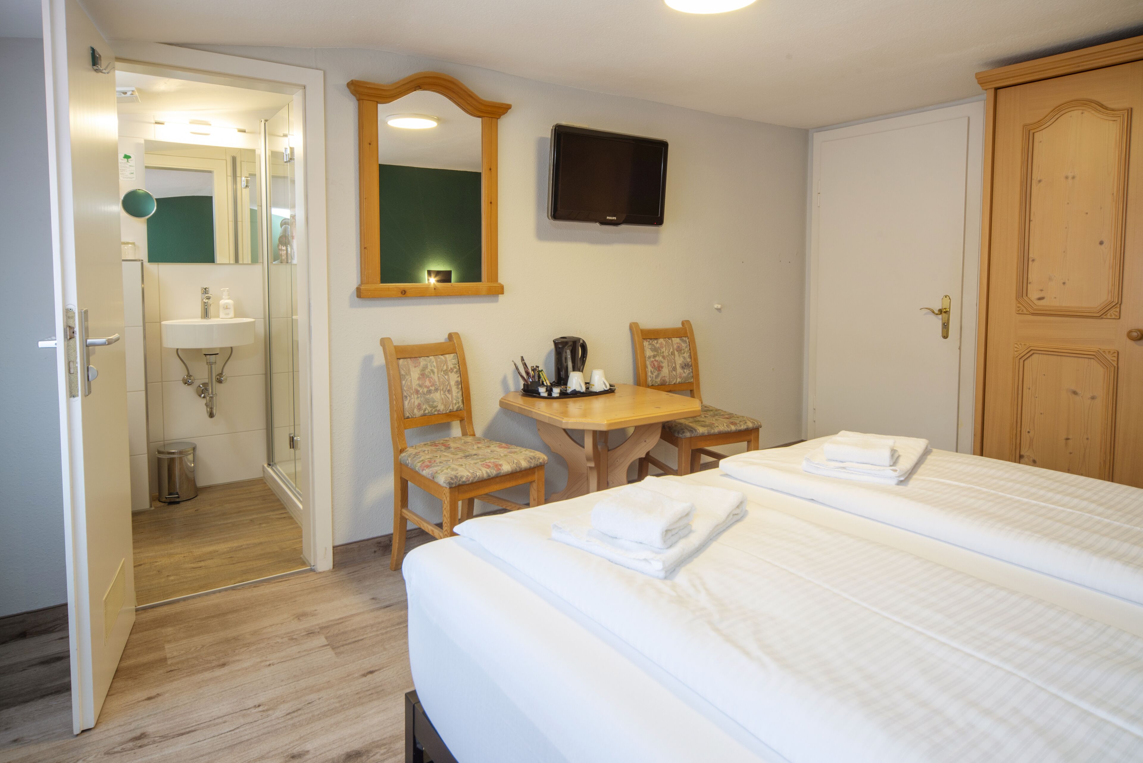 Una habitación de hotel con cama, escritorio, dos sillas, espejo, televisor y armario.