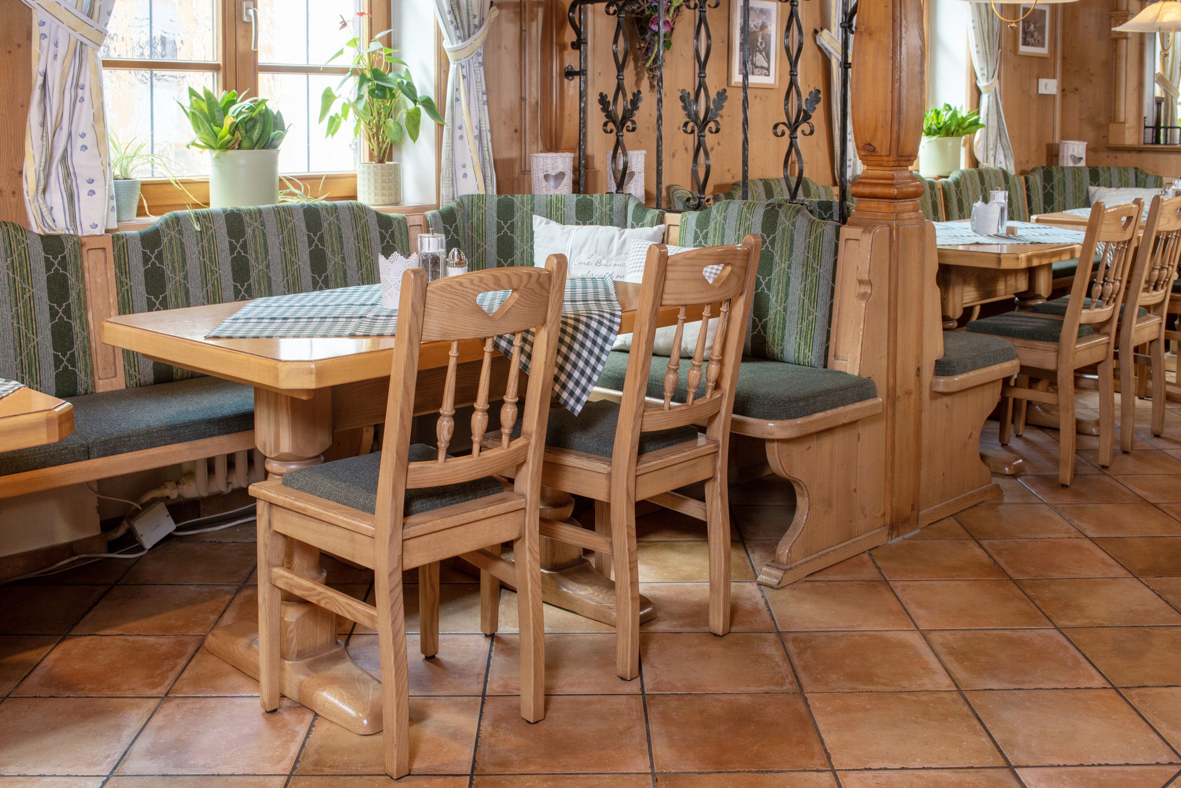Un restaurante acogedor con mobiliario de madera, cabinas tapizadas en verde y suelos de baldosas de terracota.