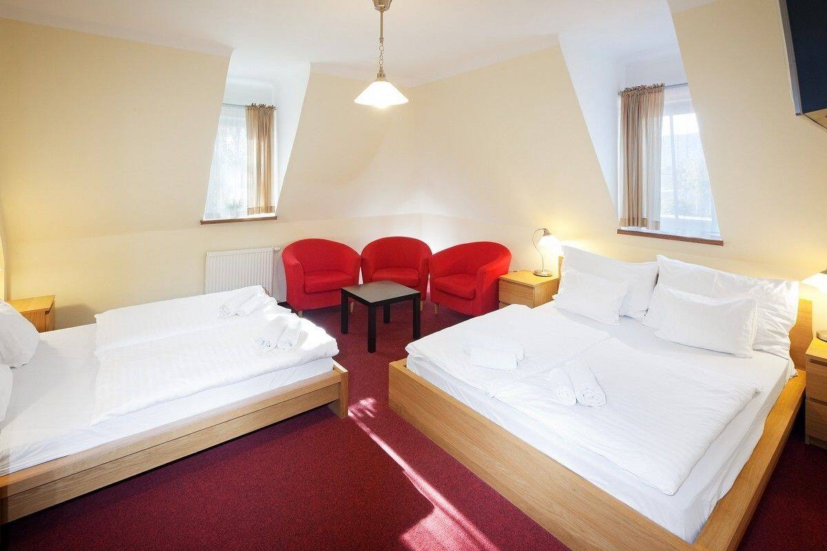 Una habitación de hotel con dos camas individuales, una mesita pequeña y tres sillas rojas.