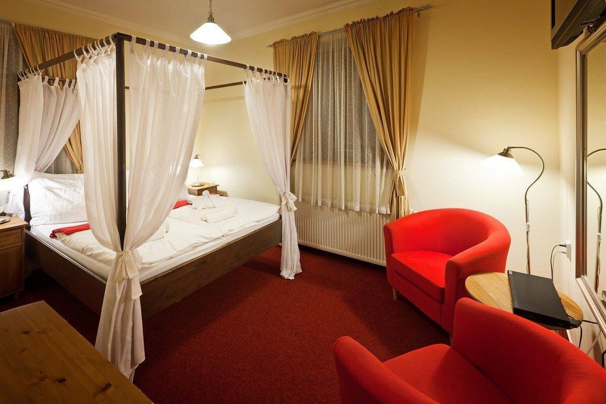 Una habitación con una cama con dosel, un sillón rojo, una mesita y una lámpara de noche.