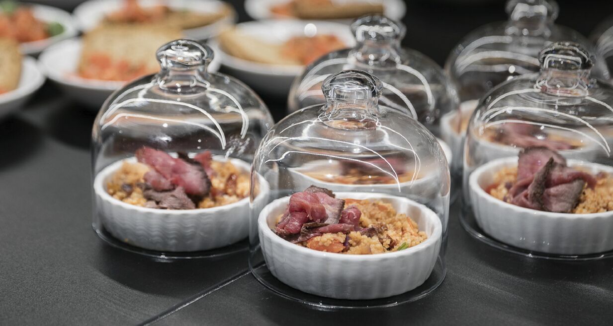 A table with several dishes covered with glass domes, containing meat and grains.