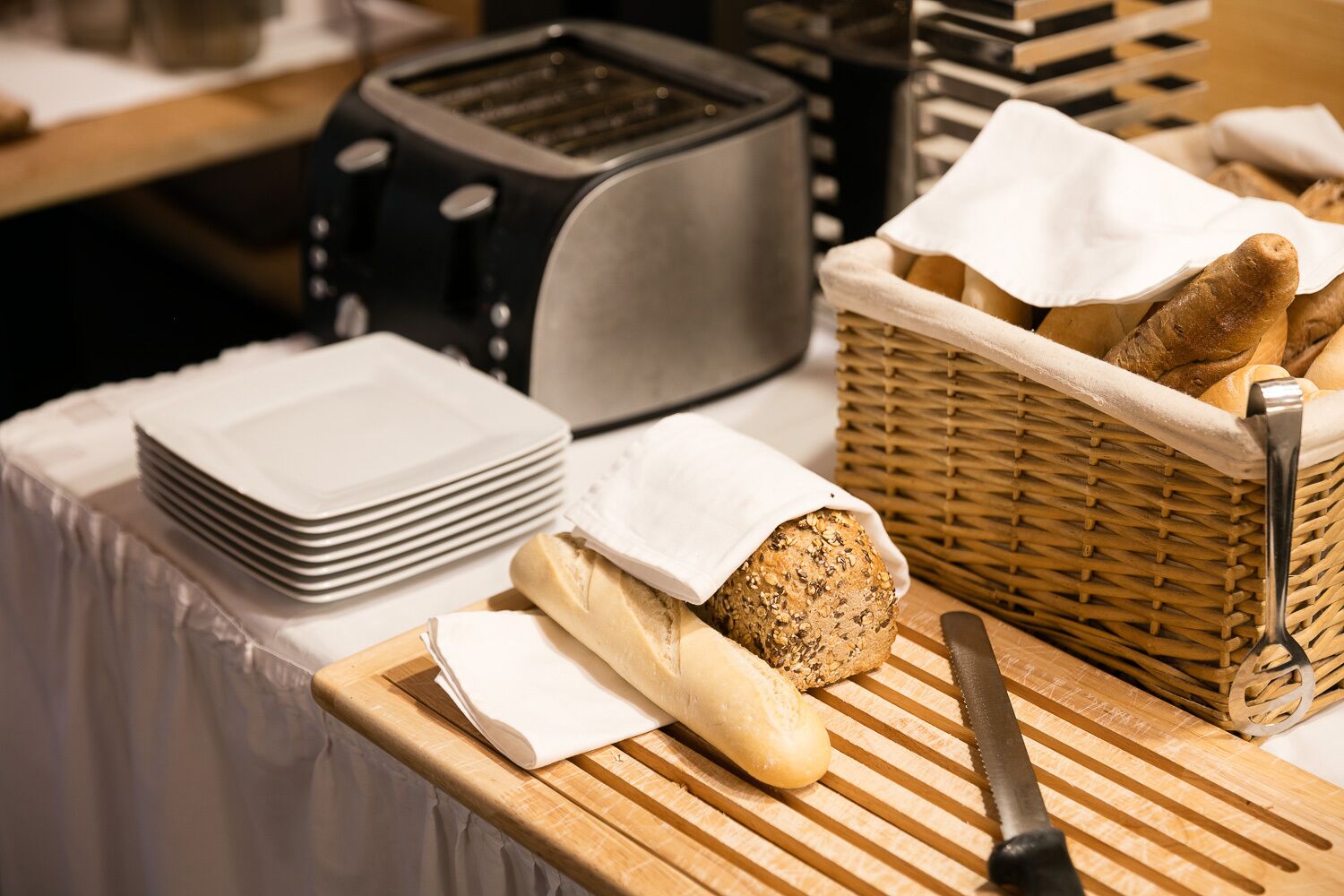 A kitchen counter with a toaster, a basket of bread, a loaf of bread, a knife, and stacked plates.