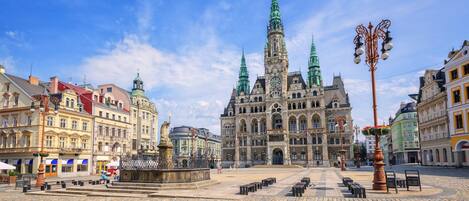 A historic square with a prominent church featuring twin spires, cobblestone pavement, and a central fountain.