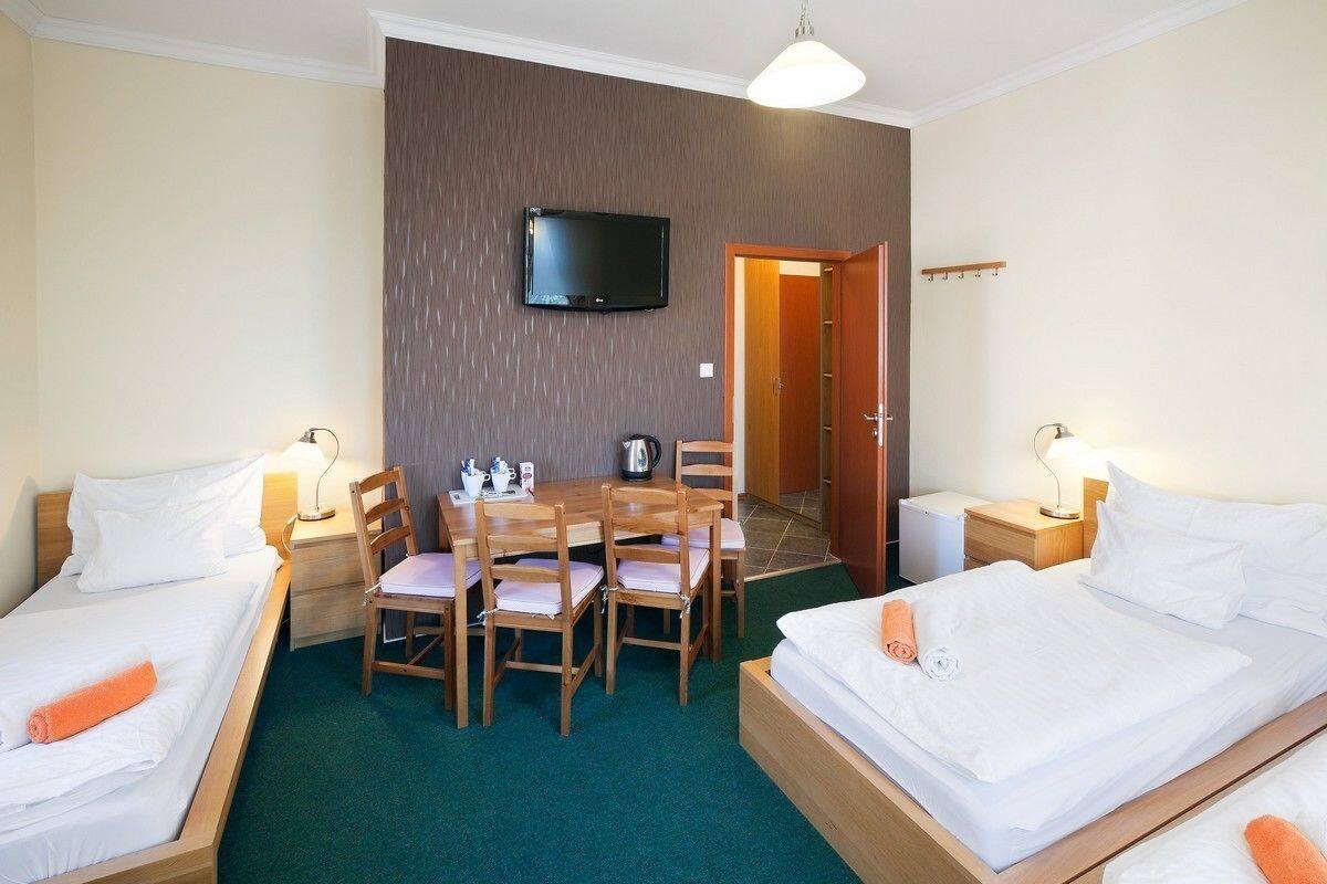Habitación de hotel con dos camas, un televisor montado en la pared, una mesa de comedor con sillas y una pequeña cocina.