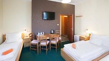 A hotel room with two beds, a TV mounted on the wall, a dining table with chairs, and a small kitchen area.