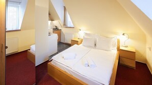 Quarto com cama grande, mesas de cabeceira, espelho e pequeno espaço de cozinha.