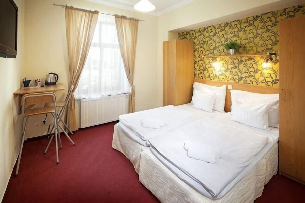Habitación de hotel con cama, escritorio, silla, radiador y ventana con cortinas.