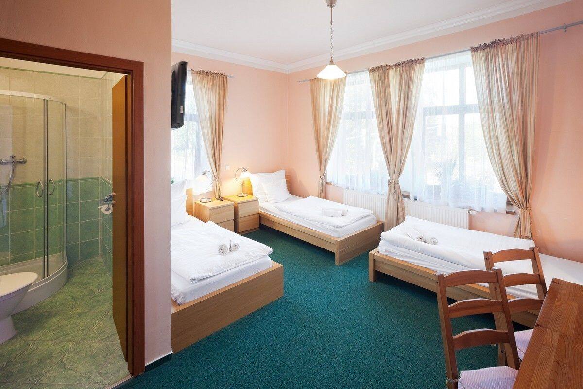 Habitación de hotel con tres camas individuales, ducha, inodoro y una silla de madera.