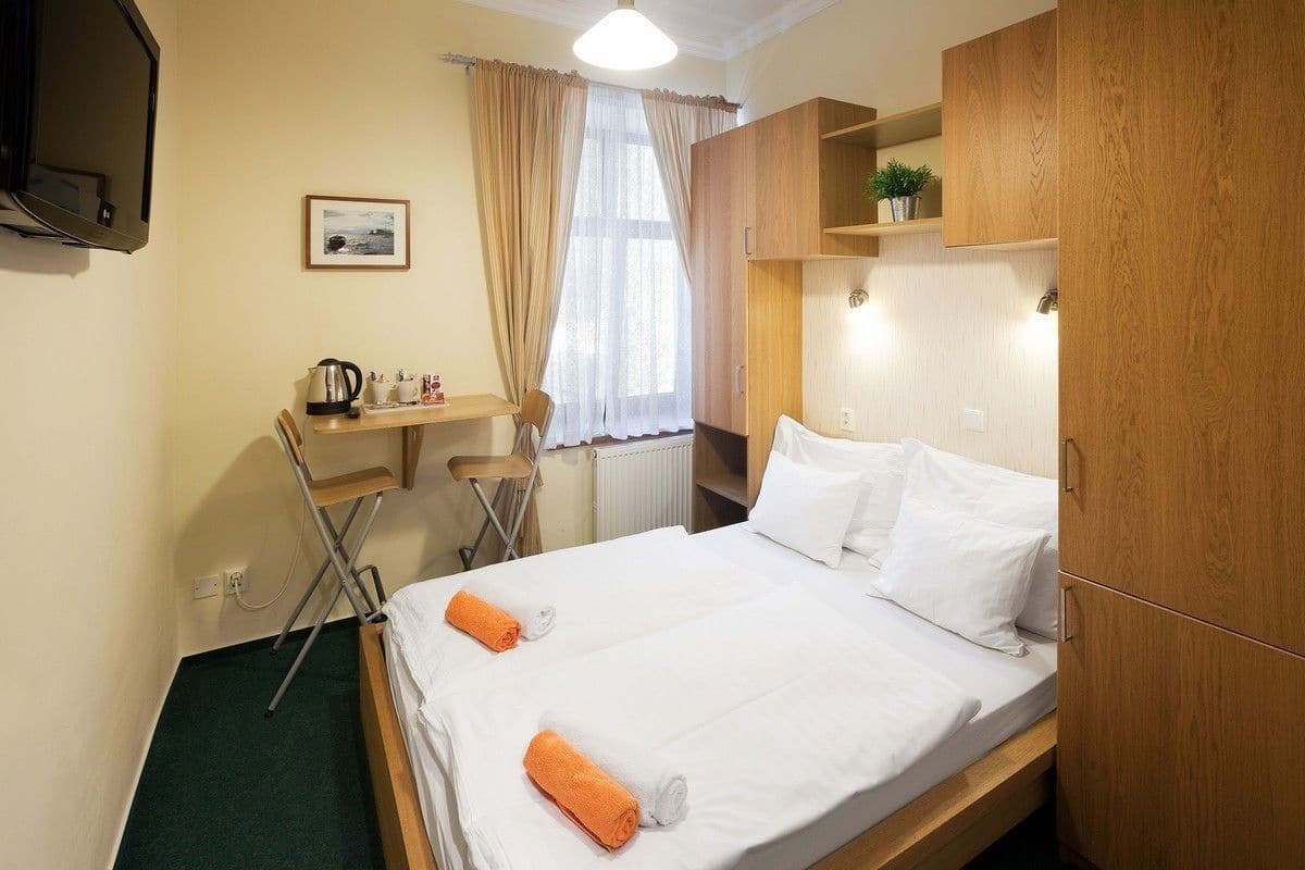 Habitación de hotel con cama, escritorio, silla, radiador y televisor montado en la pared.