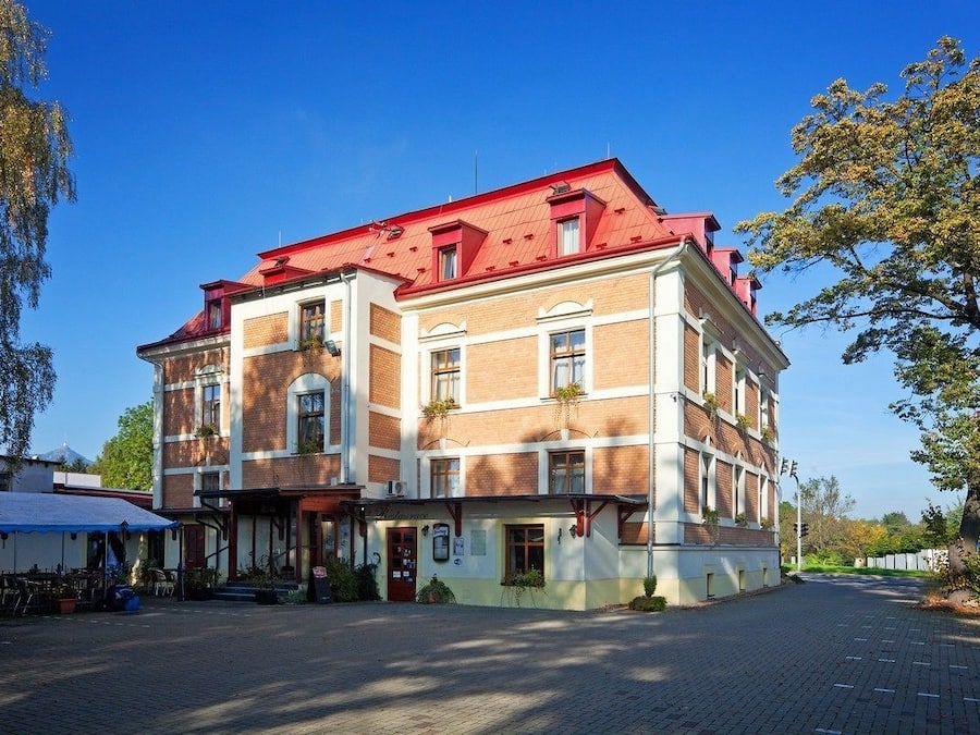 Un edificio de varios pisos con techo rojo, acceso en planta baja y un área de estar exterior visible.