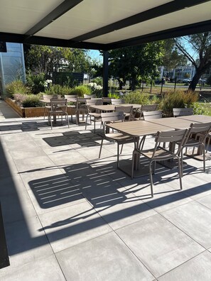 An outdoor patio area with multiple tables and chairs, surrounded by greenery and a clear sky. - The Originals Access, Hôtel Bordeaux Aéroport (Merignac)