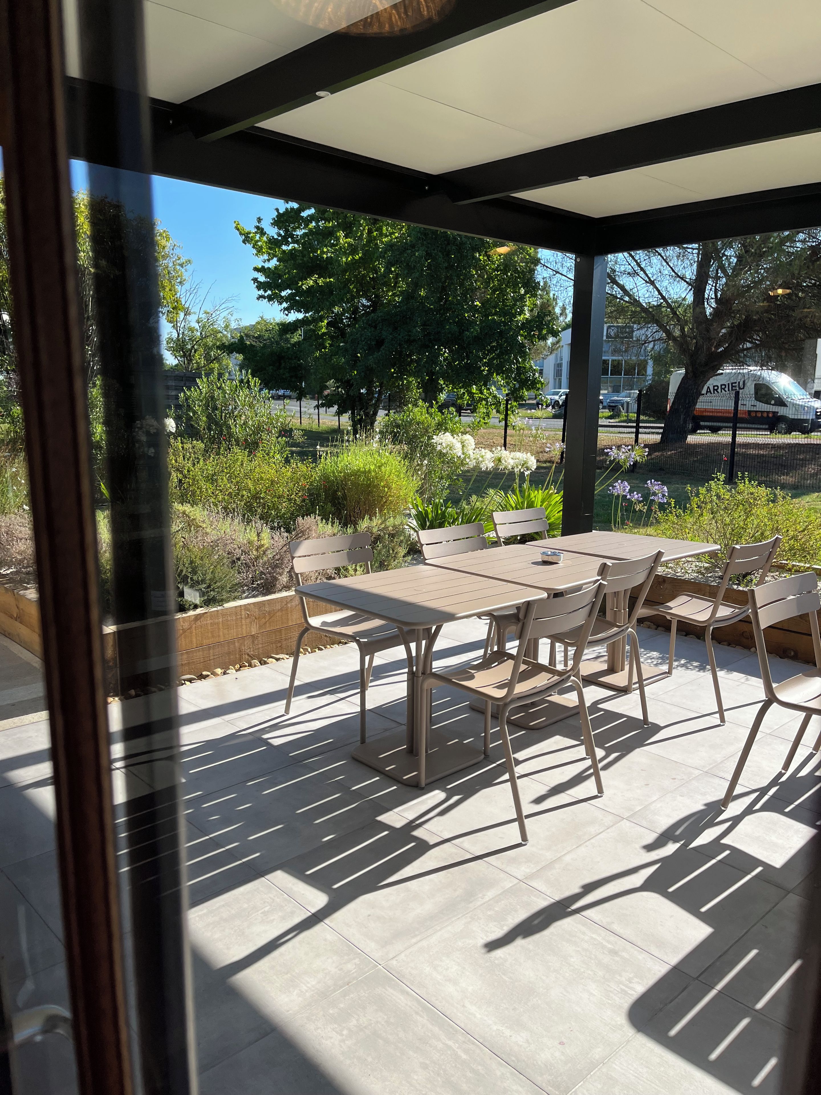 Une terrasse extérieure avec une table et des chaises, entourée de verdure et sous un ciel dégagé.