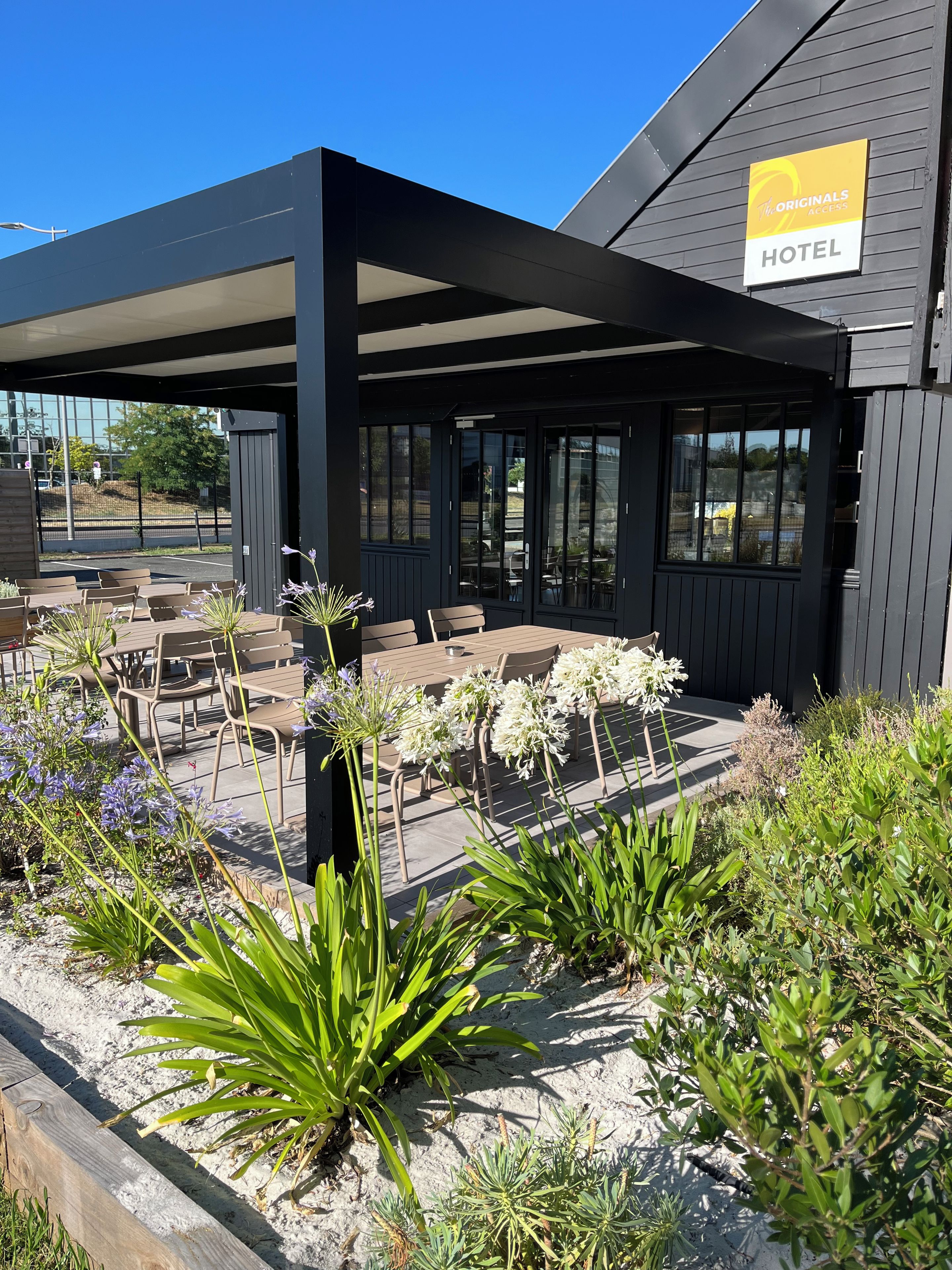 A hotel with an outdoor seating area, covered by a roof, and surrounded by plants.