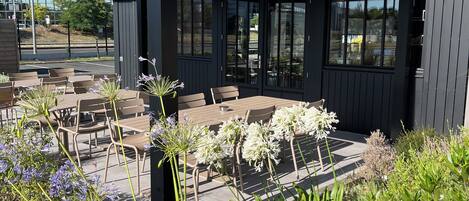 A hotel with an outdoor seating area, covered by a roof, and surrounded by plants.