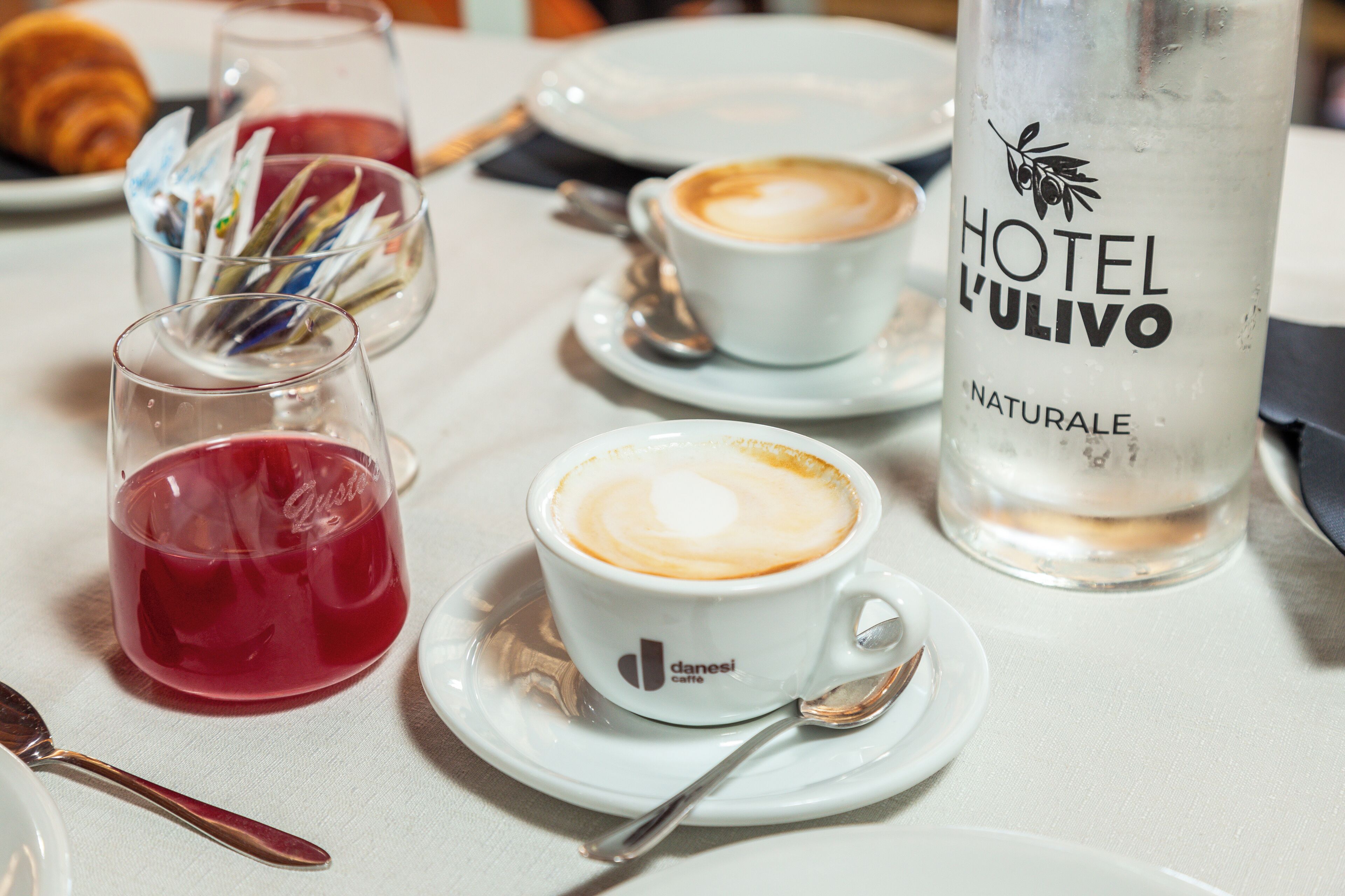 Ett bord med en kaffekopp, ett glas med en röd dryck och en flaska med etiketten "Hotel L'ulivo".