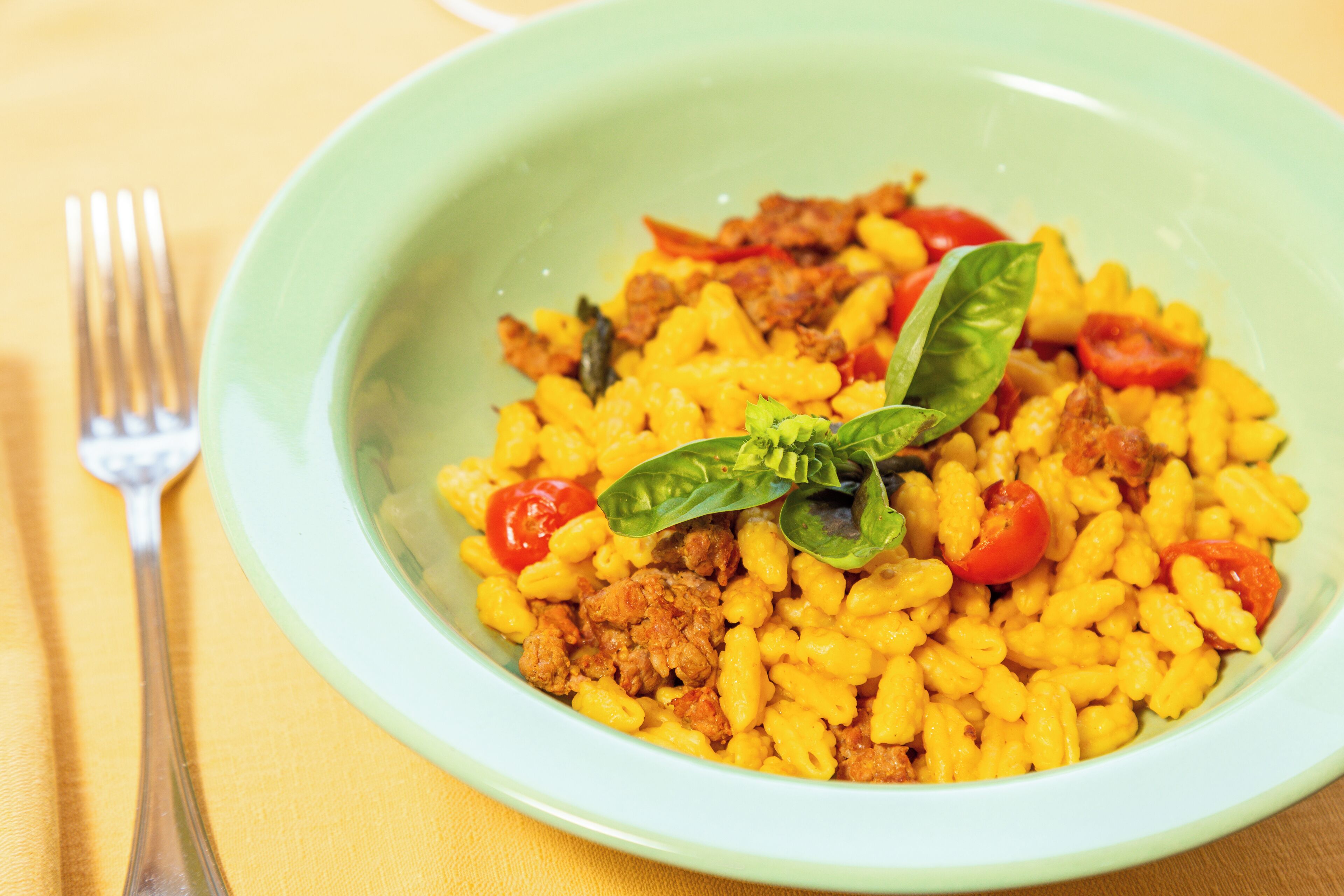 Uma tigela de massa com carne e tomate, decorada com folhas de manjericão.