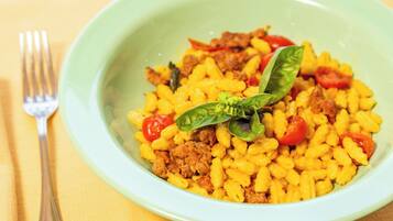 Uma tigela de massa com carne e tomate, decorada com folhas de manjericão.