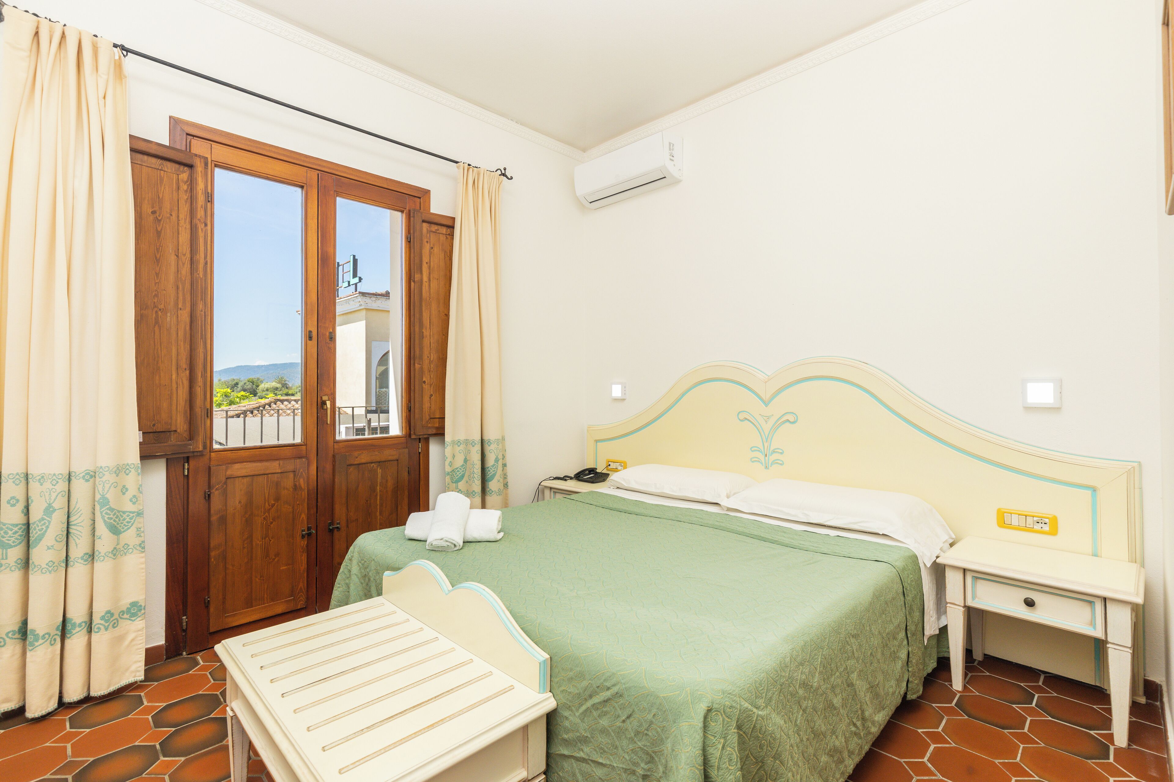 A bedroom with a bed, a nightstand, a window with curtains, and an air conditioning unit.