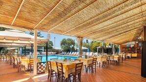 Un área de comedor al aire libre con mesas y sillas, una piscina y sombrillas.