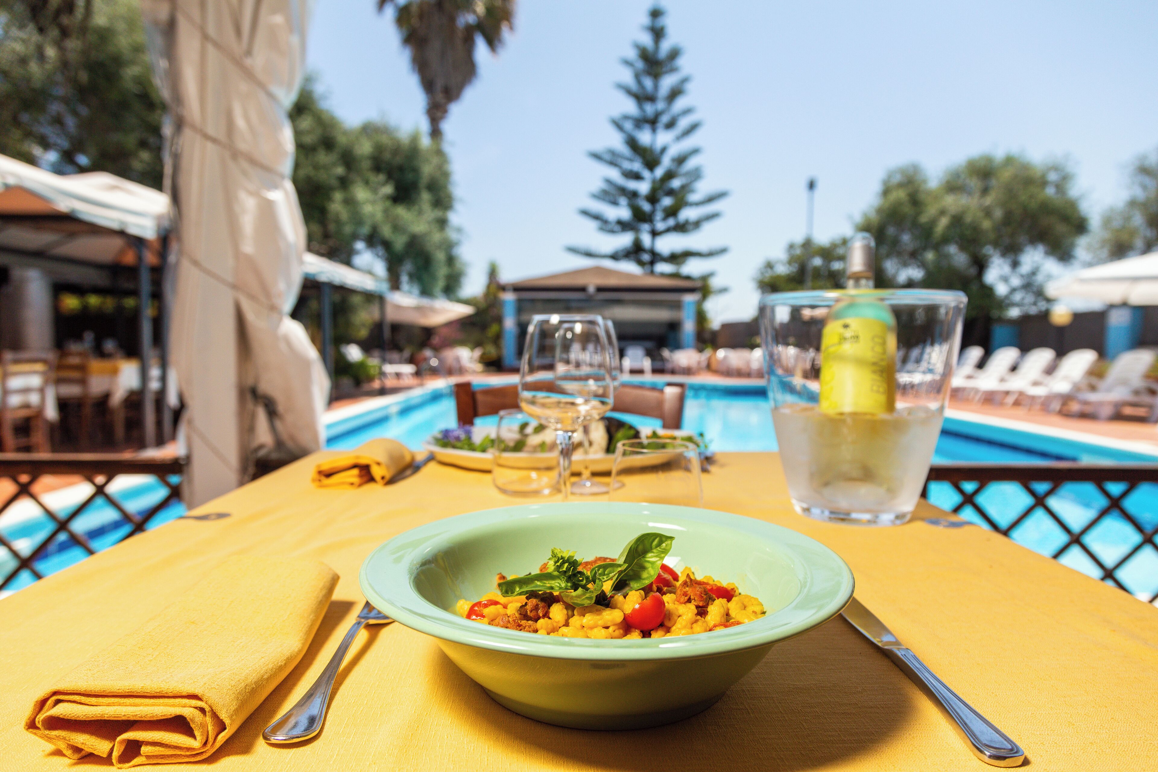 A dining table with a bowl of food, a glass of water, and a bottle of lemon.