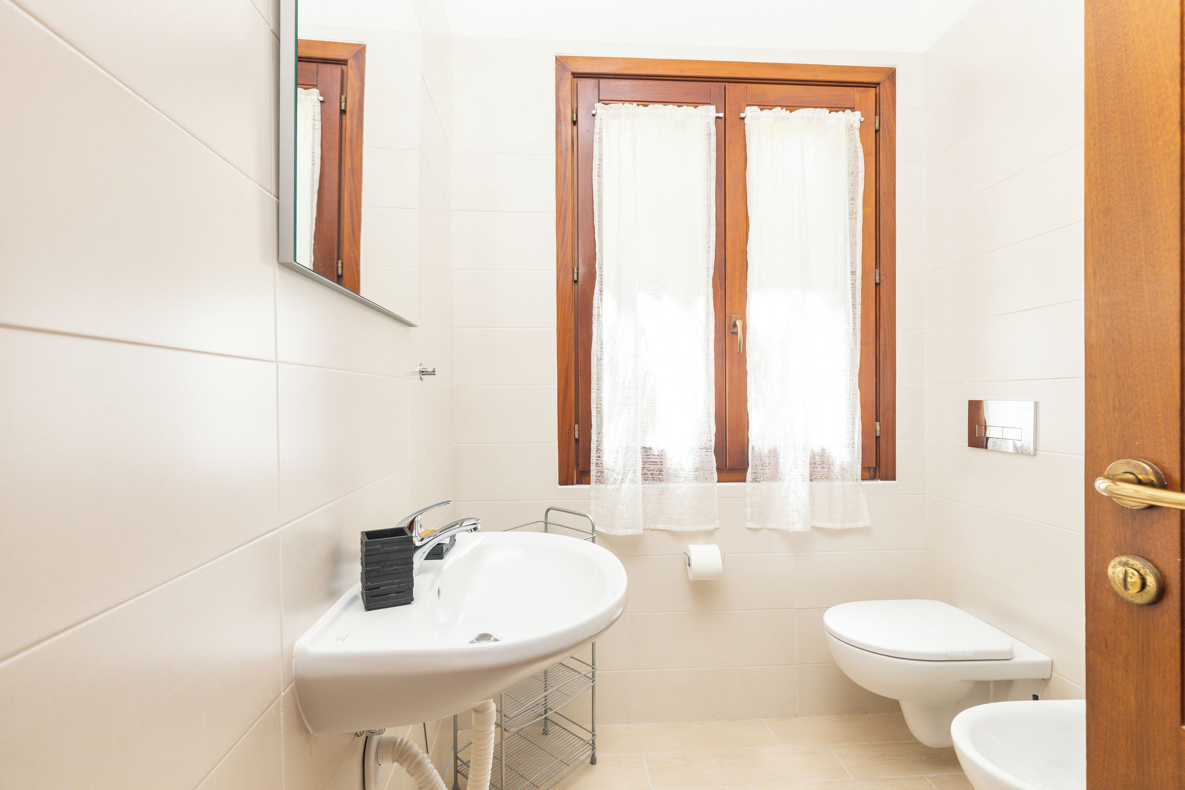 A bathroom with a sink, toilet, and window with curtains.