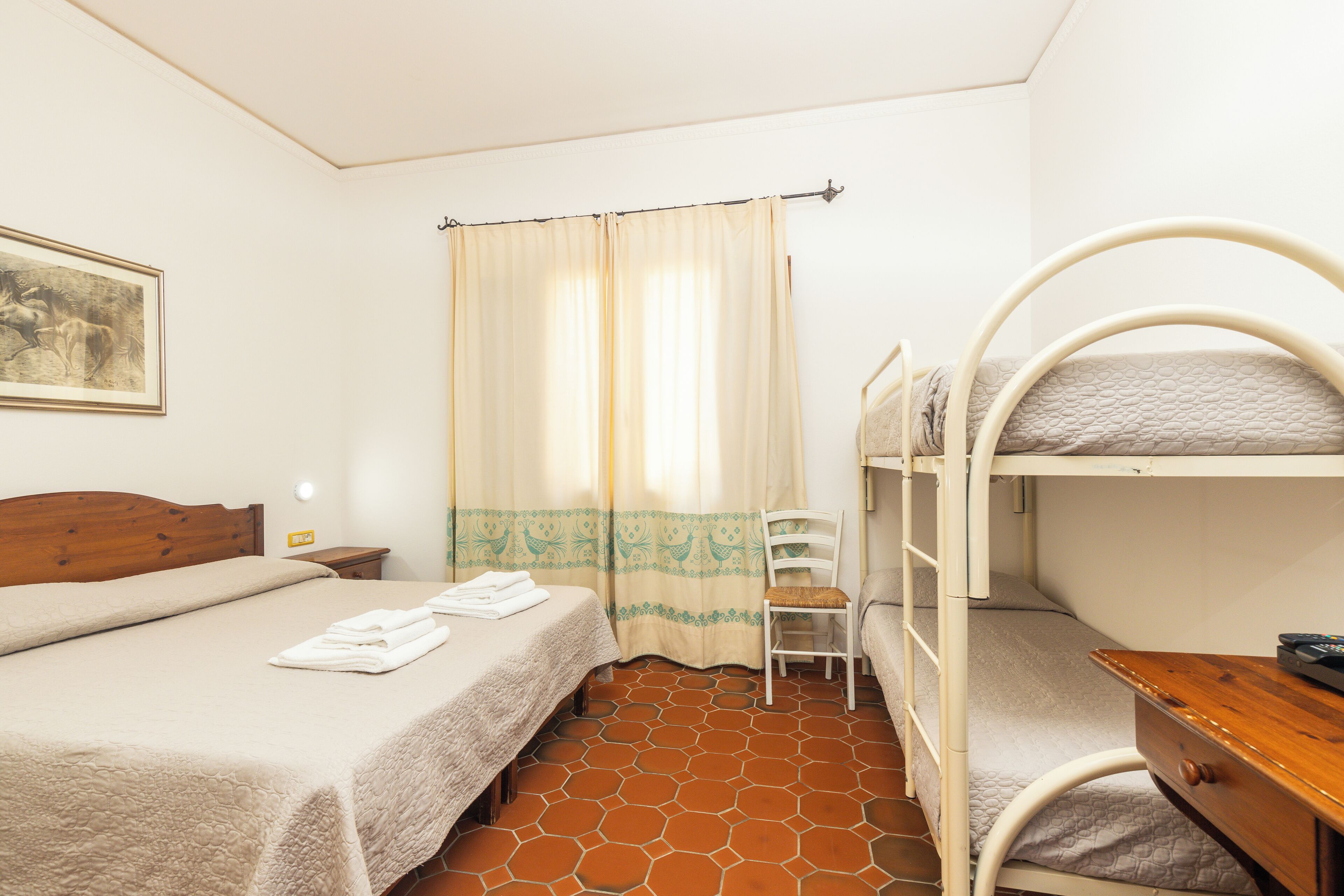 A room with a bunk bed, a single bed, a chair, a small table, and a curtain.