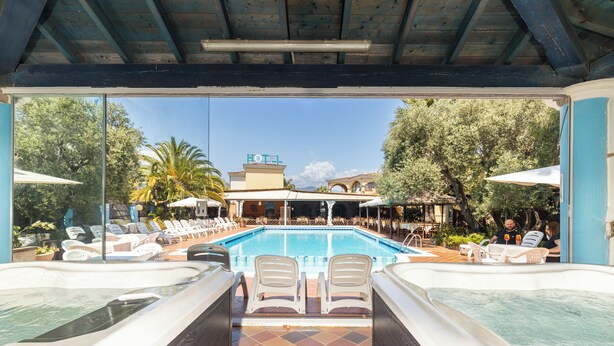 Un área de piscina con dos jacuzzis, sillas de descanso y vista a un hotel al fondo.