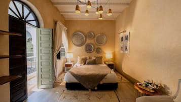 A bedroom with a bed, bedside tables, a chandelier, wall decorations, and a view through an open door.