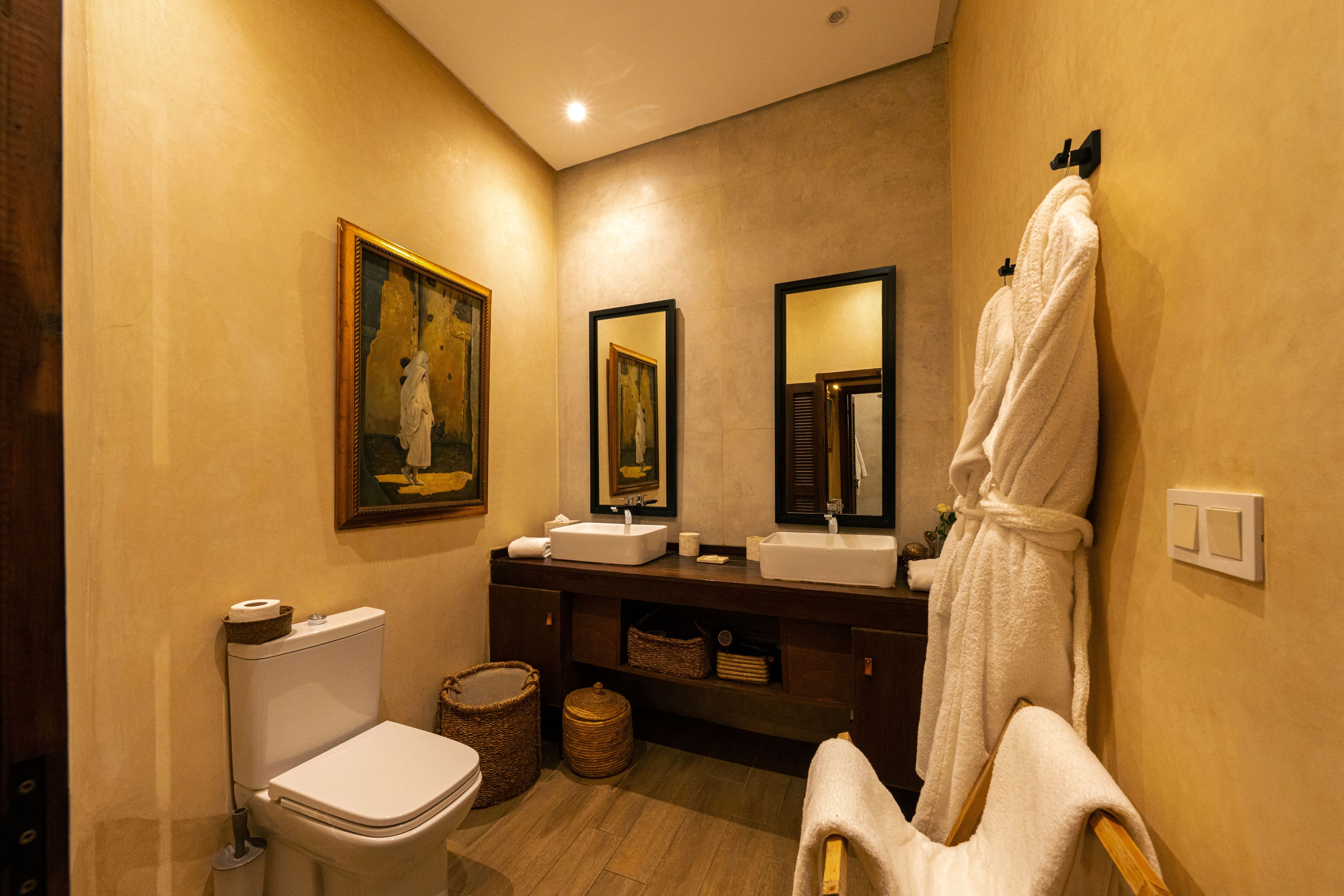 A bathroom with a toilet, bidet, sink, and a robe hanging on the wall.
