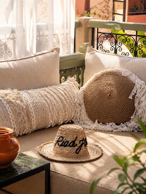 Un rincón al aire libre acogedor con un pouf tejido, un sombrero de mimbre y una maceta de terracota.