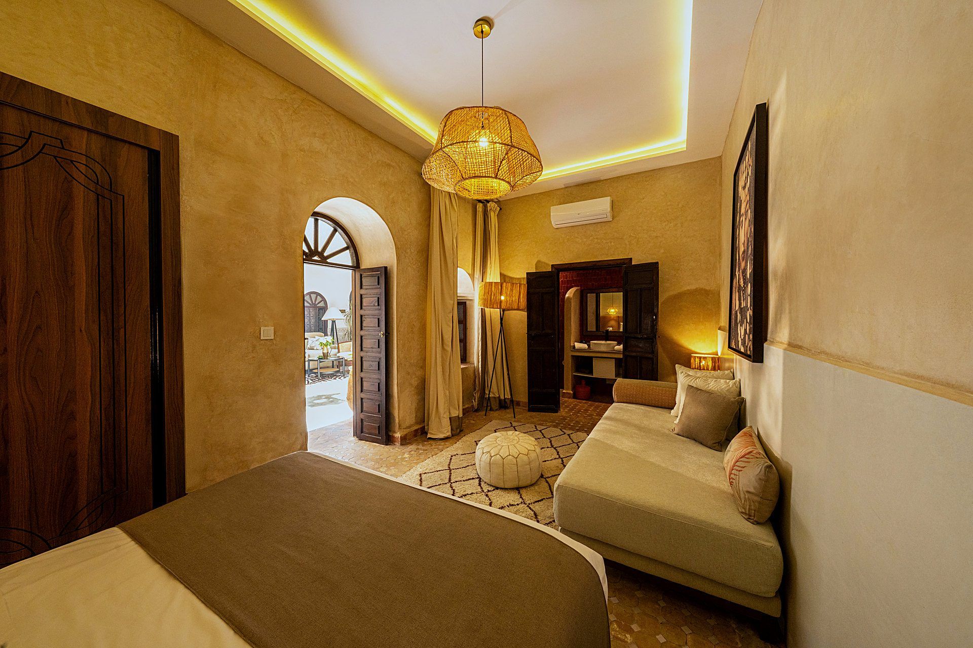 A hotel room with a bed, a sofa, a large window, and a door leading to a balcony.