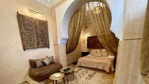 A cozy room with a brown sofa, a small round table, a patterned rug, and a bed with a canopy. - Riad Jona (Marrakech)
