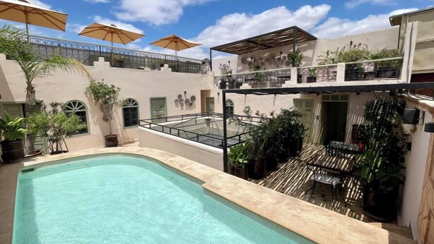 Área de piscina en la azotea con piscina azul cristalina, mobiliario exterior y plantas en macetas.