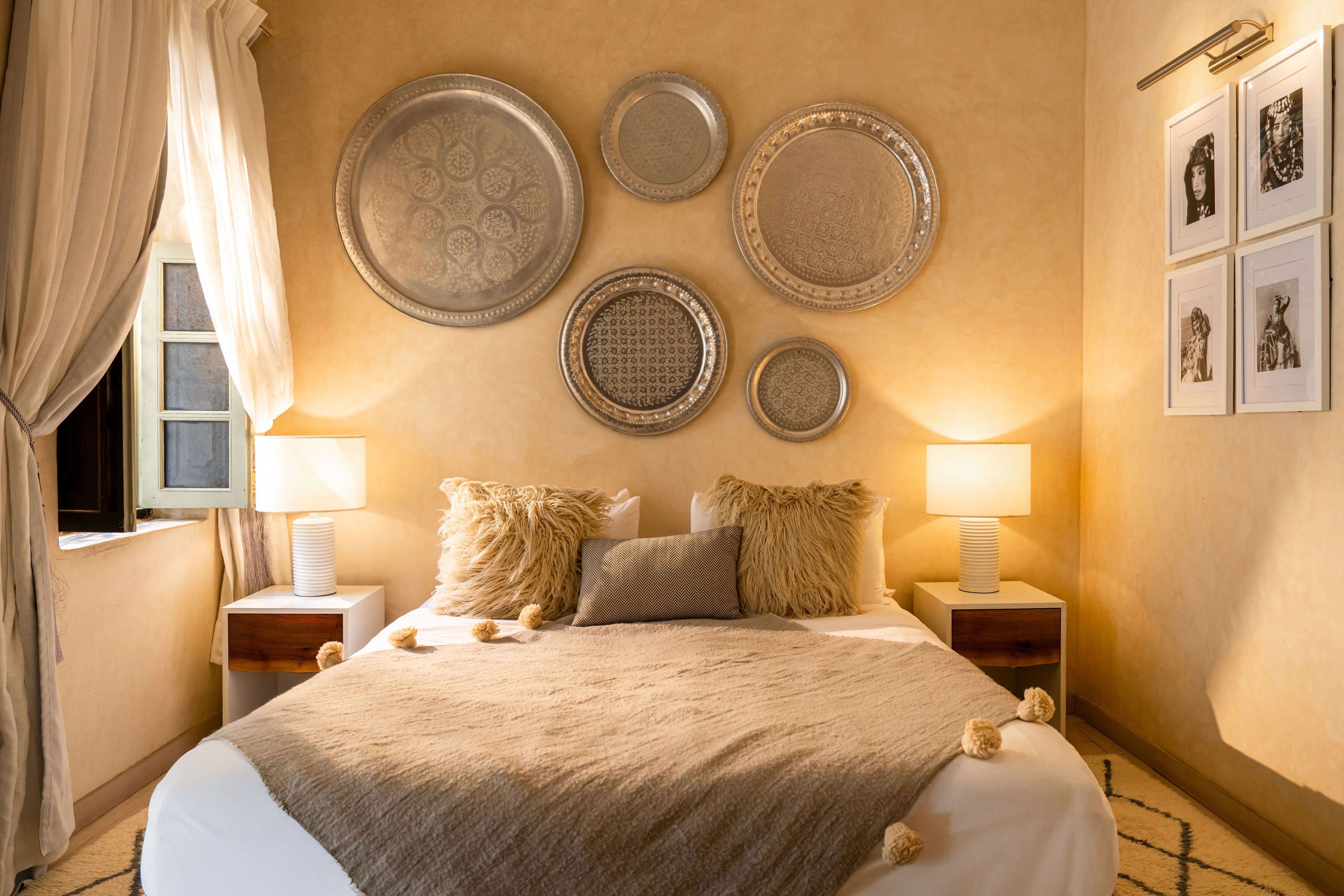 A hotel room with a bed, two bedside tables, a wall-mounted lamp, and decorative plates.