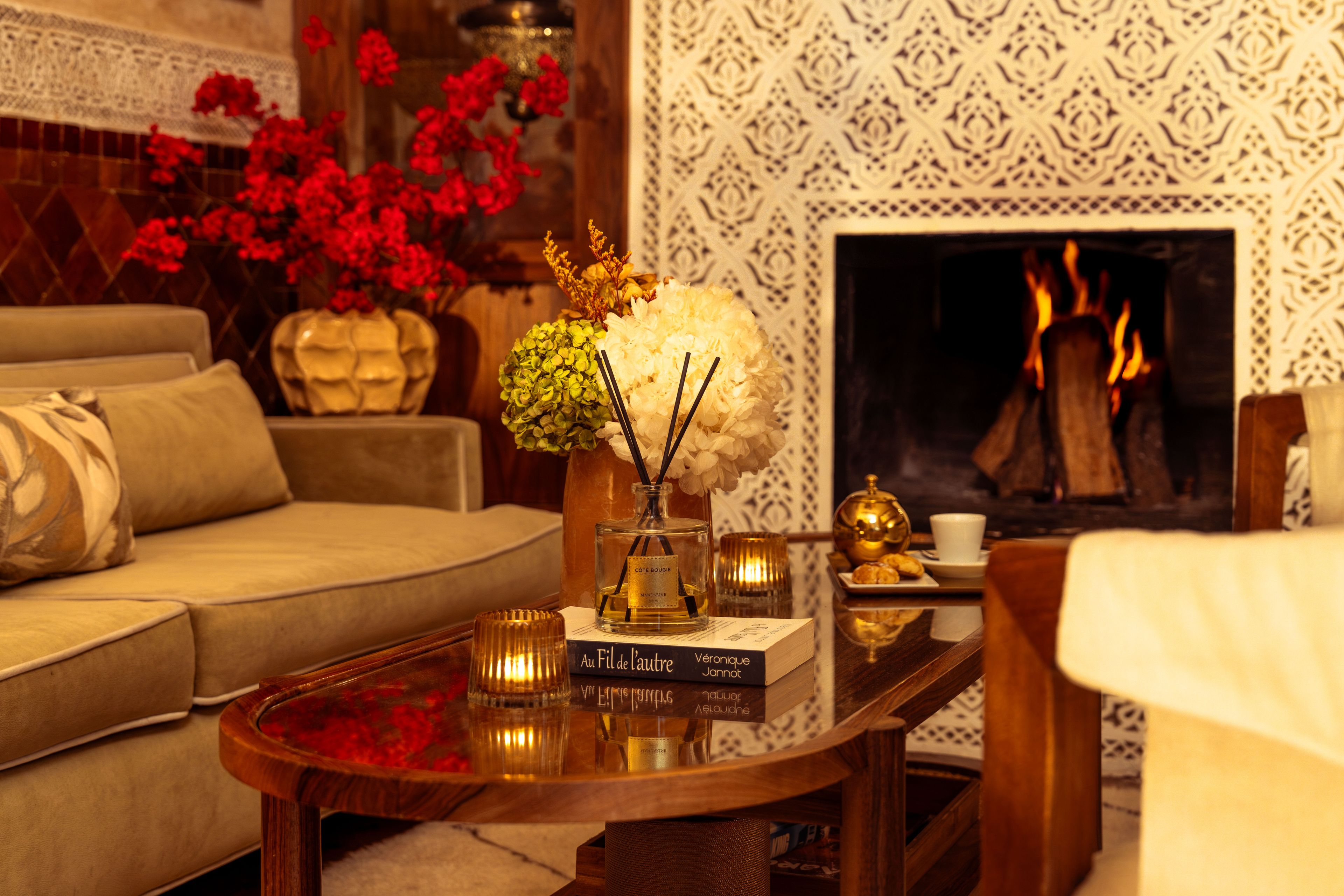 A cozy living room with a sofa, a coffee table with decorative items, a fireplace, and a patterned wall.