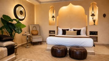 Ein Hotelzimmer mit einem großen Bett, zwei Poufs, einem Sessel, einem Beistelltisch und einer großen Pflanze.