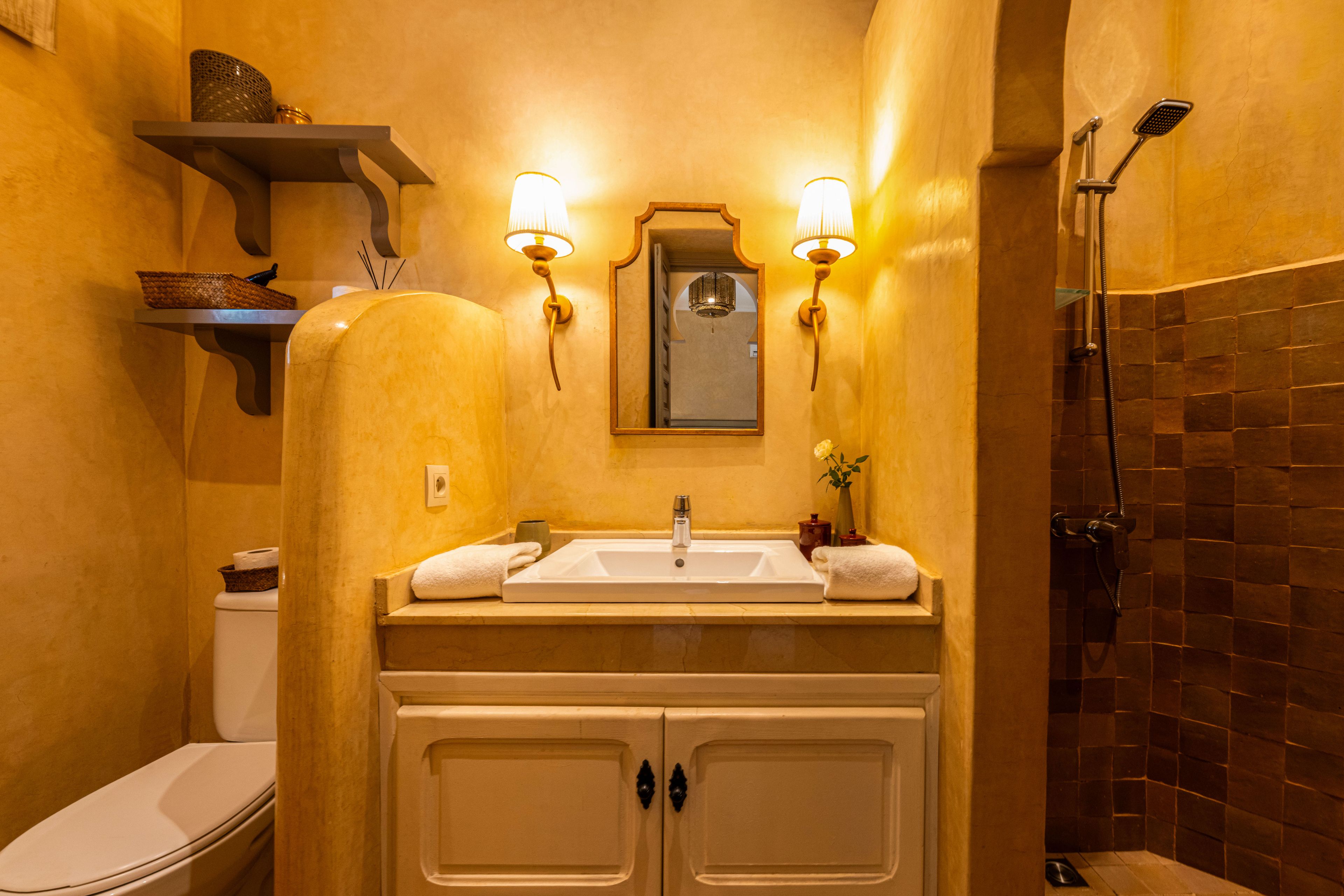 Une salle de bain avec un lavabo blanc, deux armoires, un miroir et une douche.