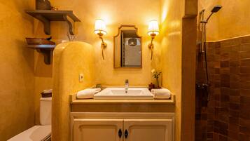 Une salle de bain avec un lavabo blanc, deux armoires, un miroir et une douche.