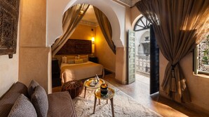 Una habitación con una cama, un sofá, una mesita con una bandeja y vistas a través de un arco.
