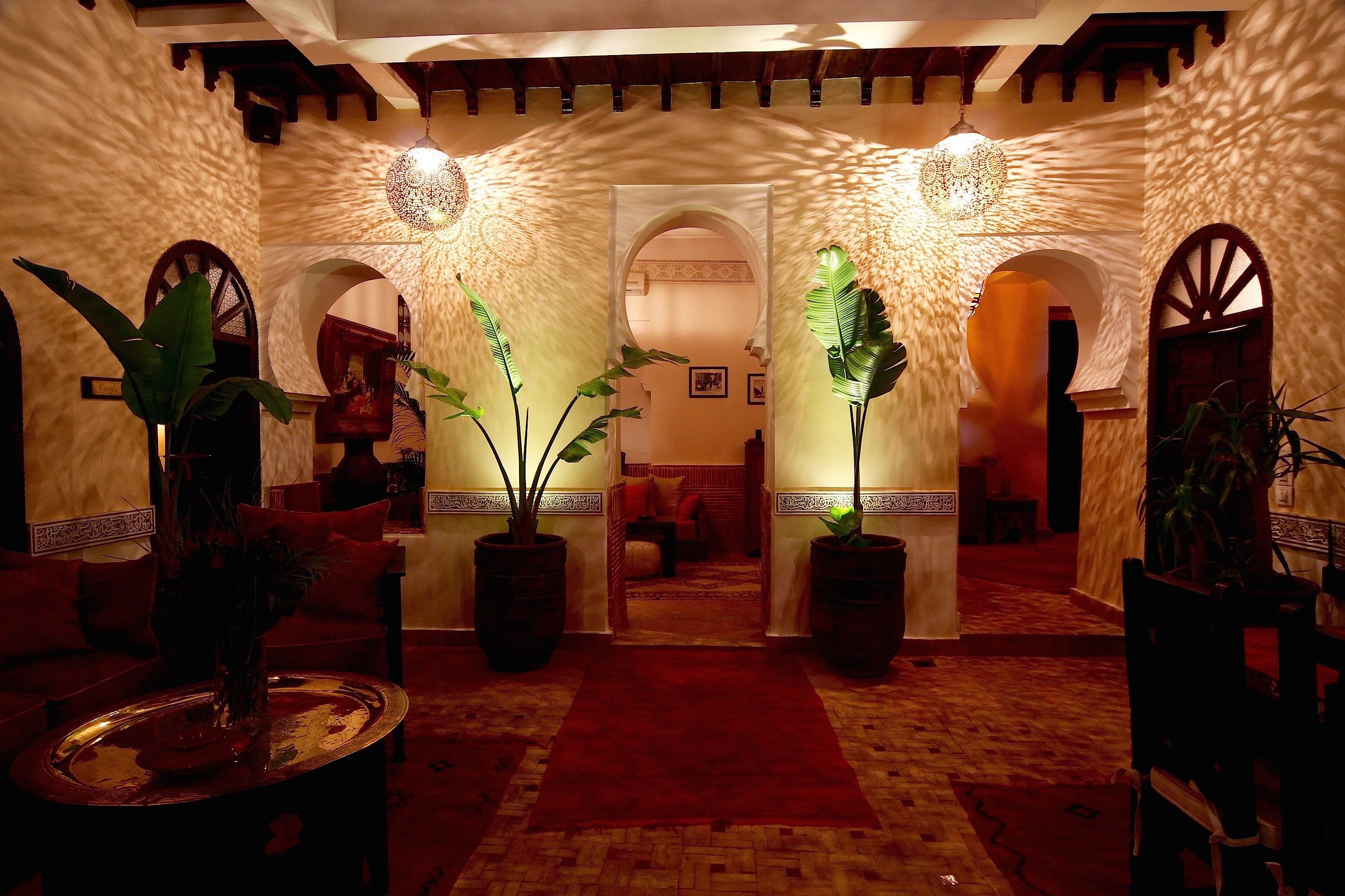 A lobby with a red carpet, large potted plants, and traditional arches.