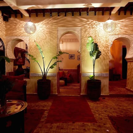 A lobby with a red carpet, large potted plants, and traditional arches.