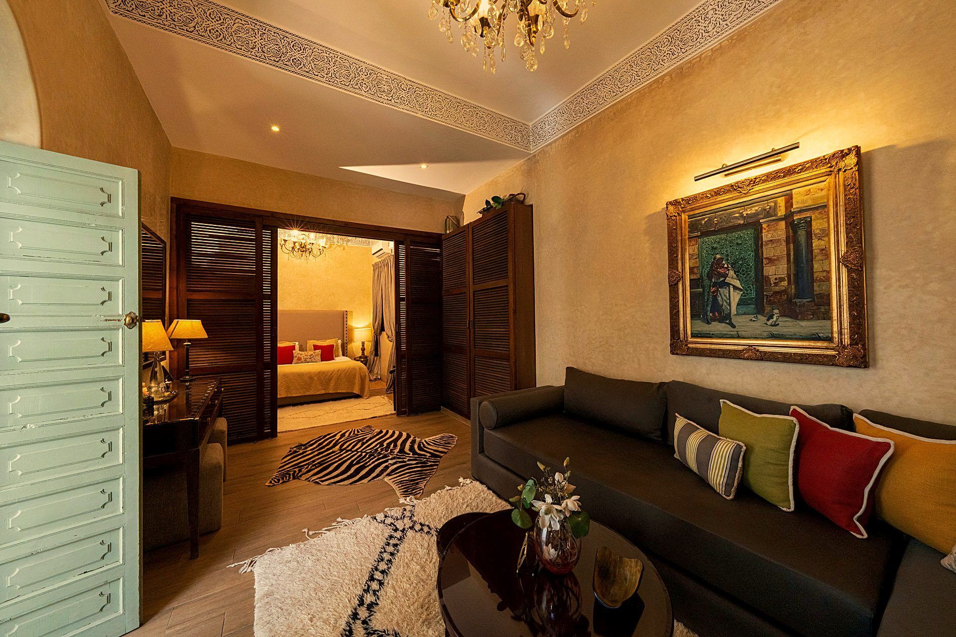 A hotel room with a bed, a sitting area with a sofa, a chandelier, and a painting on the wall.