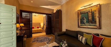 Habitación de hotel con cama, zona de estar con sofá, candelabro y un cuadro en la pared.
