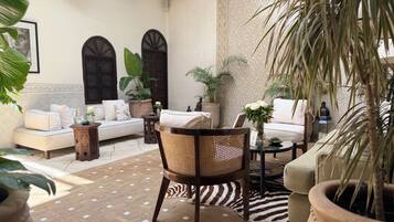Un espace de détente intérieur accueillant, avec un canapé, des fauteuils et une table basse, entouré de plantes en pot et agrémenté d’un sol à motifs.