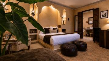 A hotel room with a large bed, a sitting area with a table, and a bathroom visible through an open door.