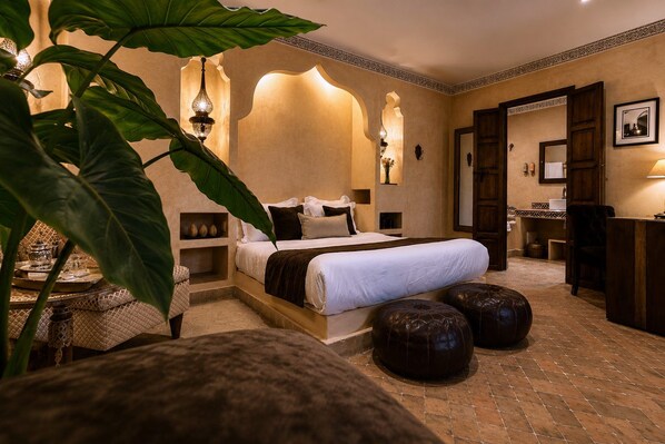 A hotel room with a large bed, a sitting area with a table, and a bathroom visible through an open door. - Riad Jona (Marrakech)