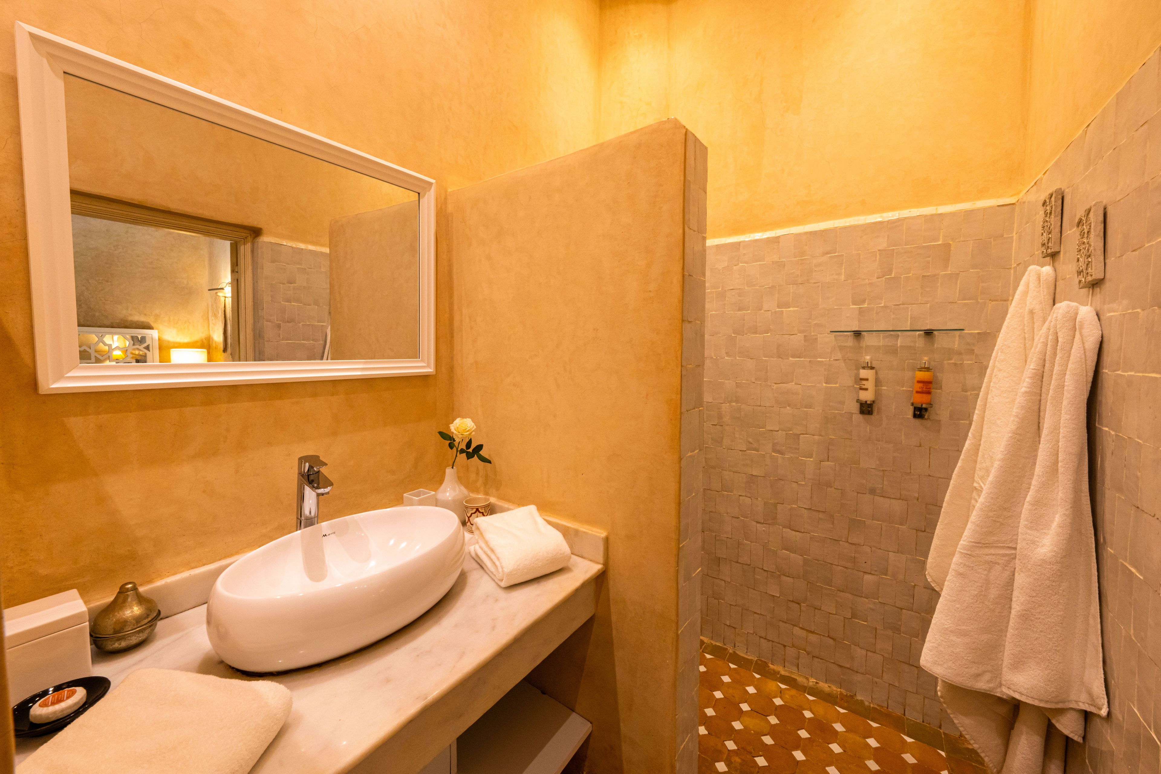 A bathroom with a large mirror, a sink, a towel rack, and a shower area.