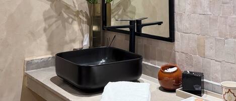 Un baño con espejo, un jarrón con flores, un lavabo negro y una toalla sobre la encimera.
