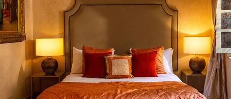 Quarto de hotel com uma cama grande, duas luminárias de cabeceira, um quadro na parede e uma janela com cortinas.