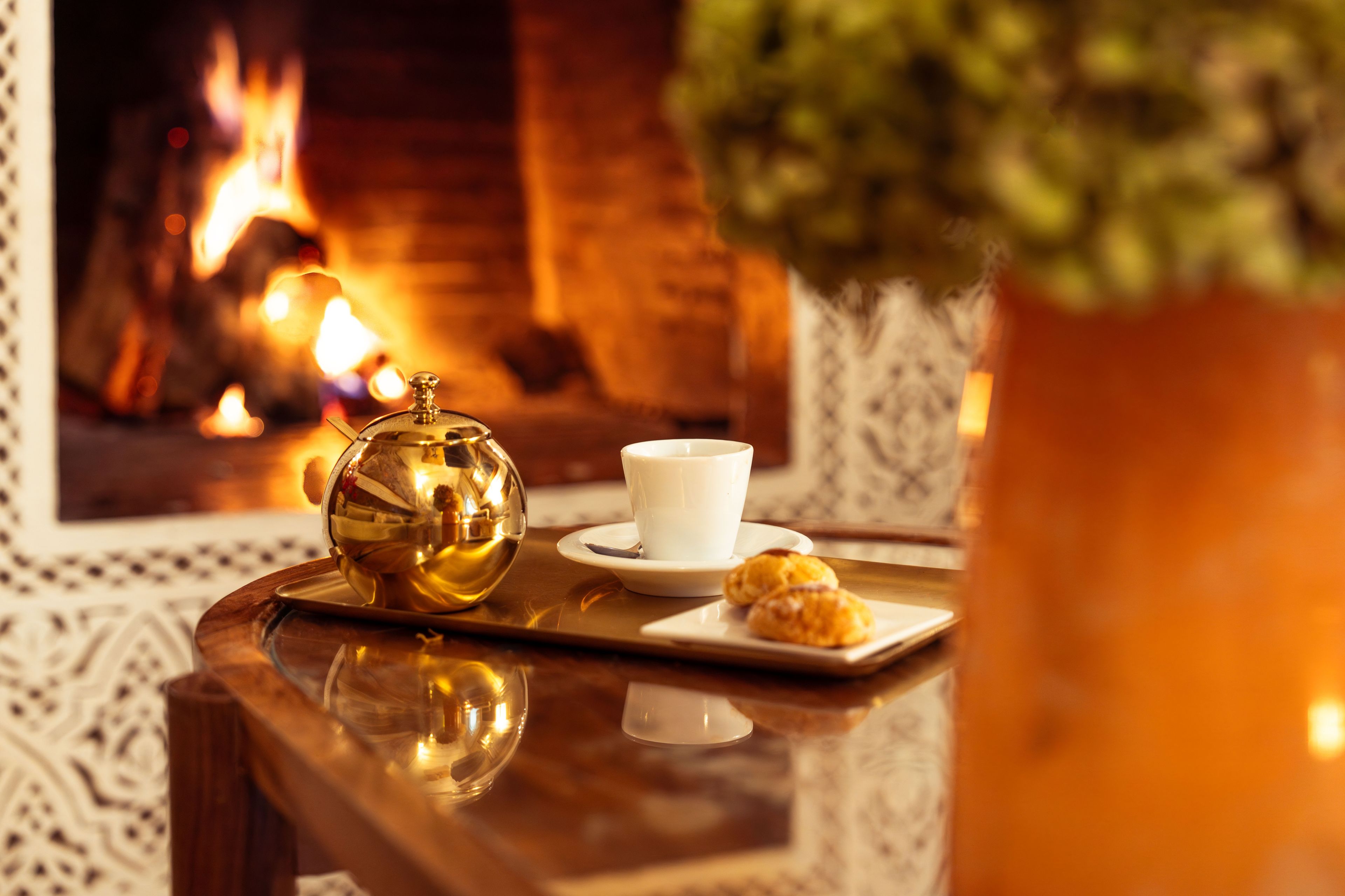 A tray with a teapot, a cup, and pastries on a table with a fireplace in the background.
